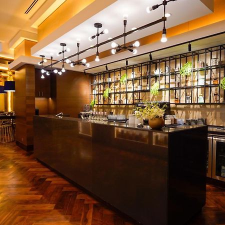 Hotel Jabal Omar Hyatt Regency Makkah La La Mecca Esterno foto The photo shows a modern bar area in a restaurant. The bar features a sleek, dark countertop and is backed by a decorative arrangement of shelves that holds various bottles and plants. The lighting is warm and stylish, with multiple hanging pendant l