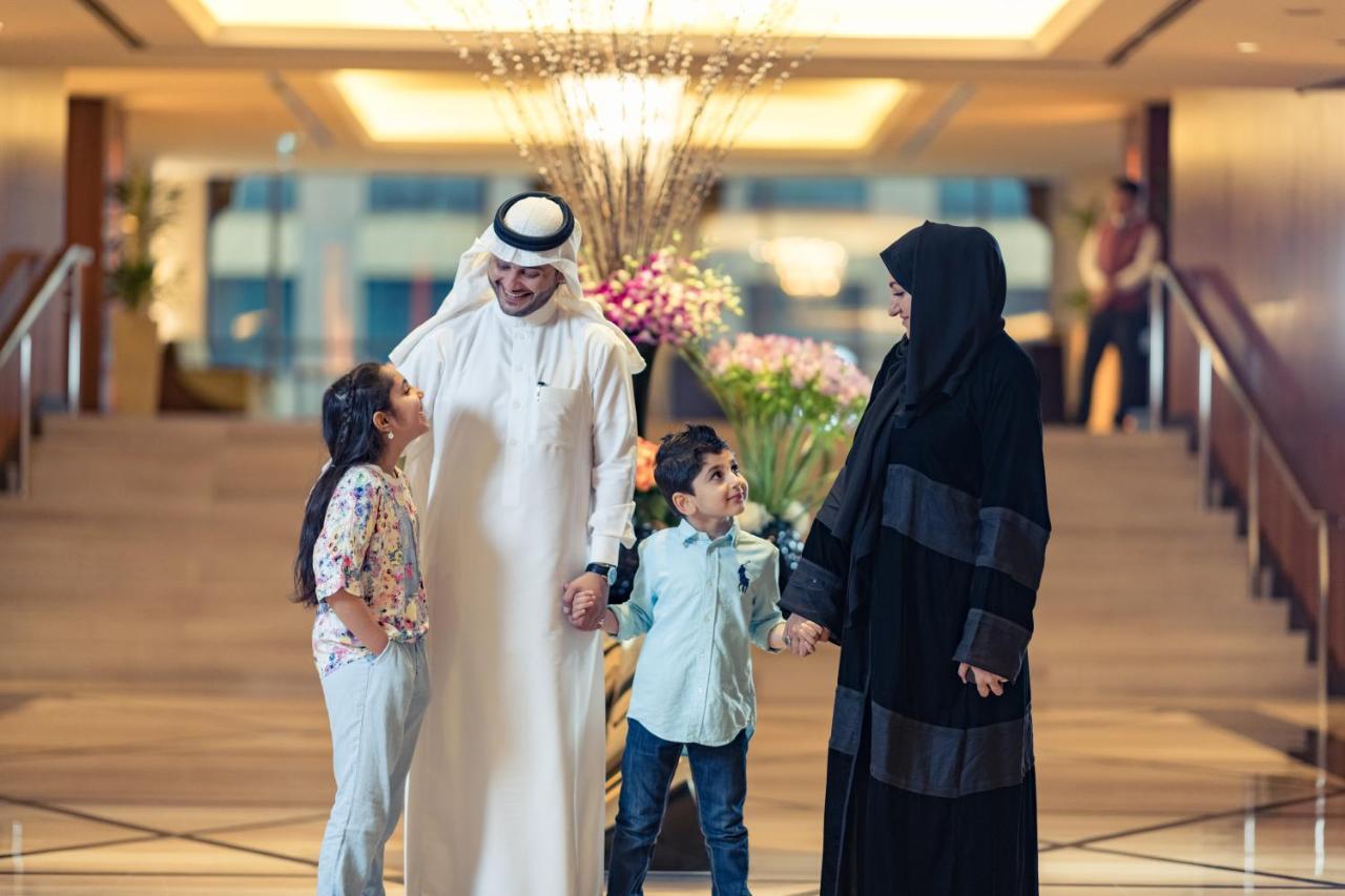 Hotel Jabal Omar Hyatt Regency Makkah La La Mecca Esterno foto The photo shows a family in a hotel lobby. There are two children, a boy and a girl, standing between their parents. The girl is smiling and looking up at her father, who is wearing traditional white attire and a headscarf. The boy is also smiling an