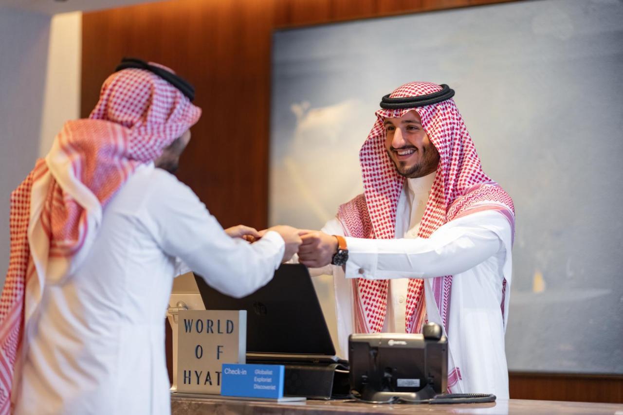 Hotel Jabal Omar Hyatt Regency Makkah La La Mecca Esterno foto The photo shows a scene at a hotel reception desk. A hotel staff member, dressed in traditional attire, is smiling and handing something to a guest, who is also wearing traditional clothing. The guest appears to be receiving a key or a document. The 