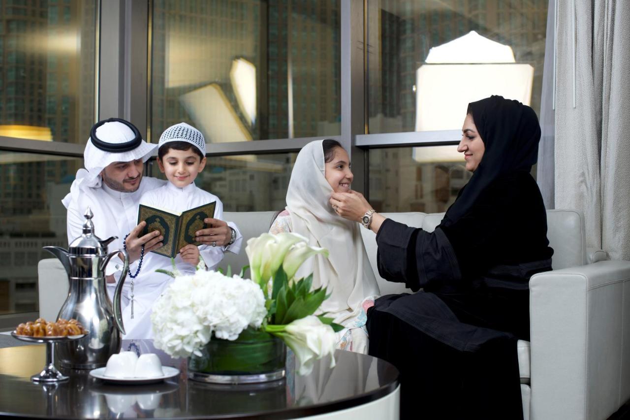 Hotel Jabal Omar Hyatt Regency Makkah La La Mecca Esterno foto The photo depicts a family gathering in a modern, well-furnished setting. A man and a boy, both dressed in traditional attire, are engaged in reading from a book, likely the Quran. A woman, wearing a hijab and a black abaya, is sitting next to them, 