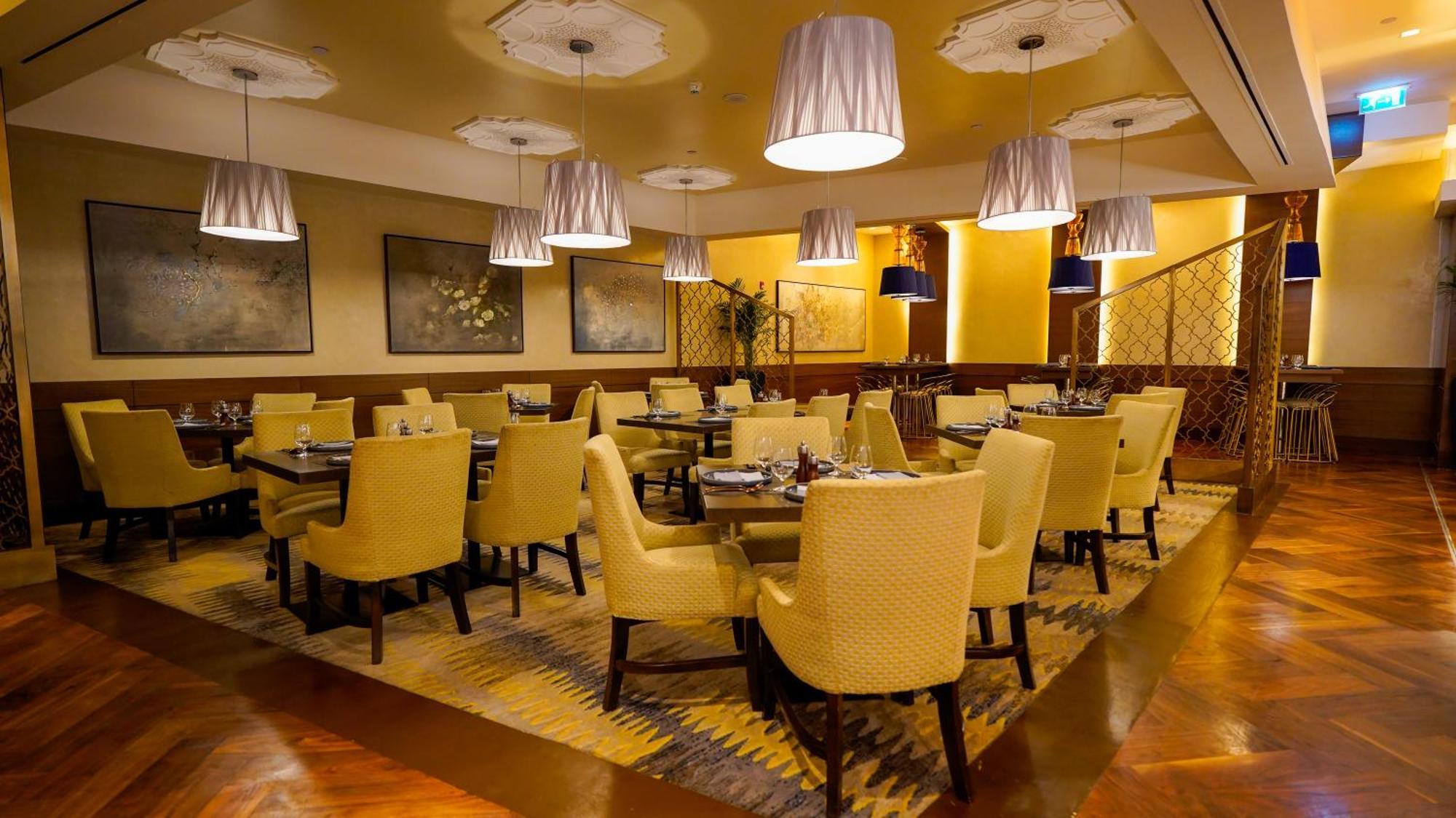 Hotel Jabal Omar Hyatt Regency Makkah La La Mecca Esterno foto The photo shows an elegant restaurant interior. There are several tables arranged with yellow upholstered chairs, creating a warm and inviting atmosphere. Soft lighting is provided by modern pendant lamps hanging from the ceiling. The floor features 