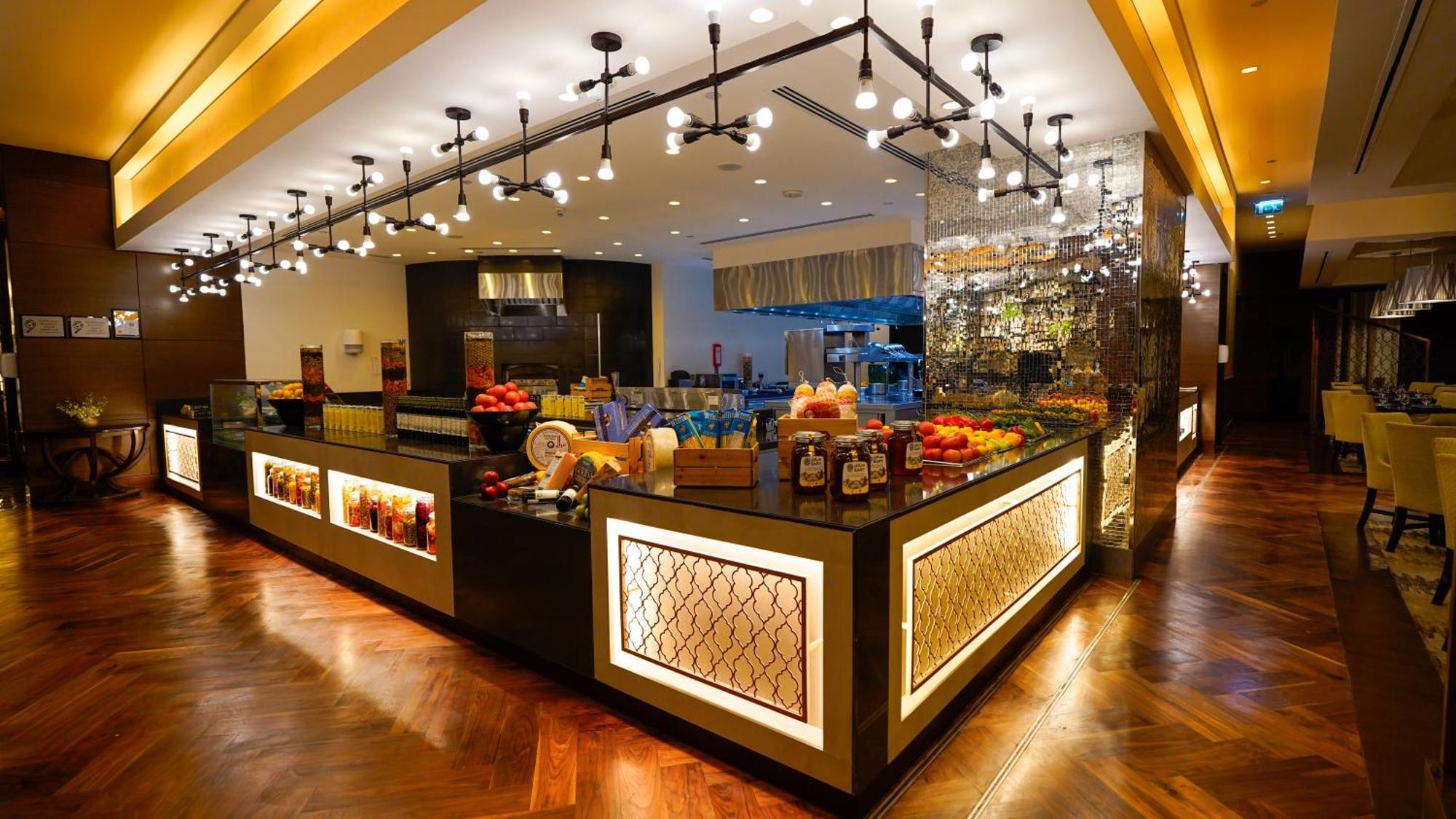 Hotel Jabal Omar Hyatt Regency Makkah La La Mecca Esterno foto The photo shows a stylish and modern buffet area in a restaurant or hotel. The design features a sleek counter with various food items displayed, including fresh fruits. The space is well-lit with pendant lights hanging from the ceiling, creating a w