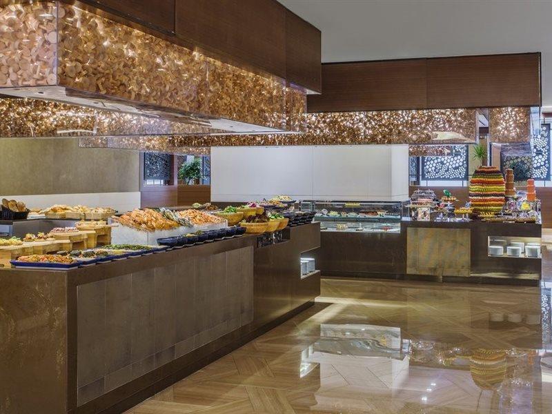Hotel Jabal Omar Hyatt Regency Makkah La La Mecca Esterno foto The photo shows a stylish buffet area, likely in a restaurant or hotel. There are several food displays arranged on long tables with shiny surfaces. The buffet features a variety of items, which may include pastries, bread, and other dishes. The area