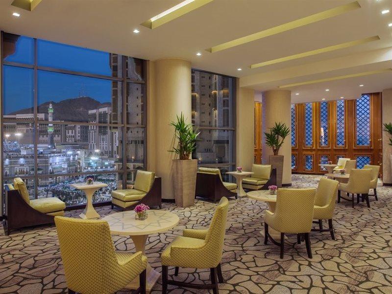 Hotel Jabal Omar Hyatt Regency Makkah La La Mecca Esterno foto The photo shows a modern, well-lit lounge or reception area. It features several small round tables surrounded by comfortable chairs, all in a soft yellow upholstery. The flooring is composed of stone tiles, adding a natural element to the decor. Lar