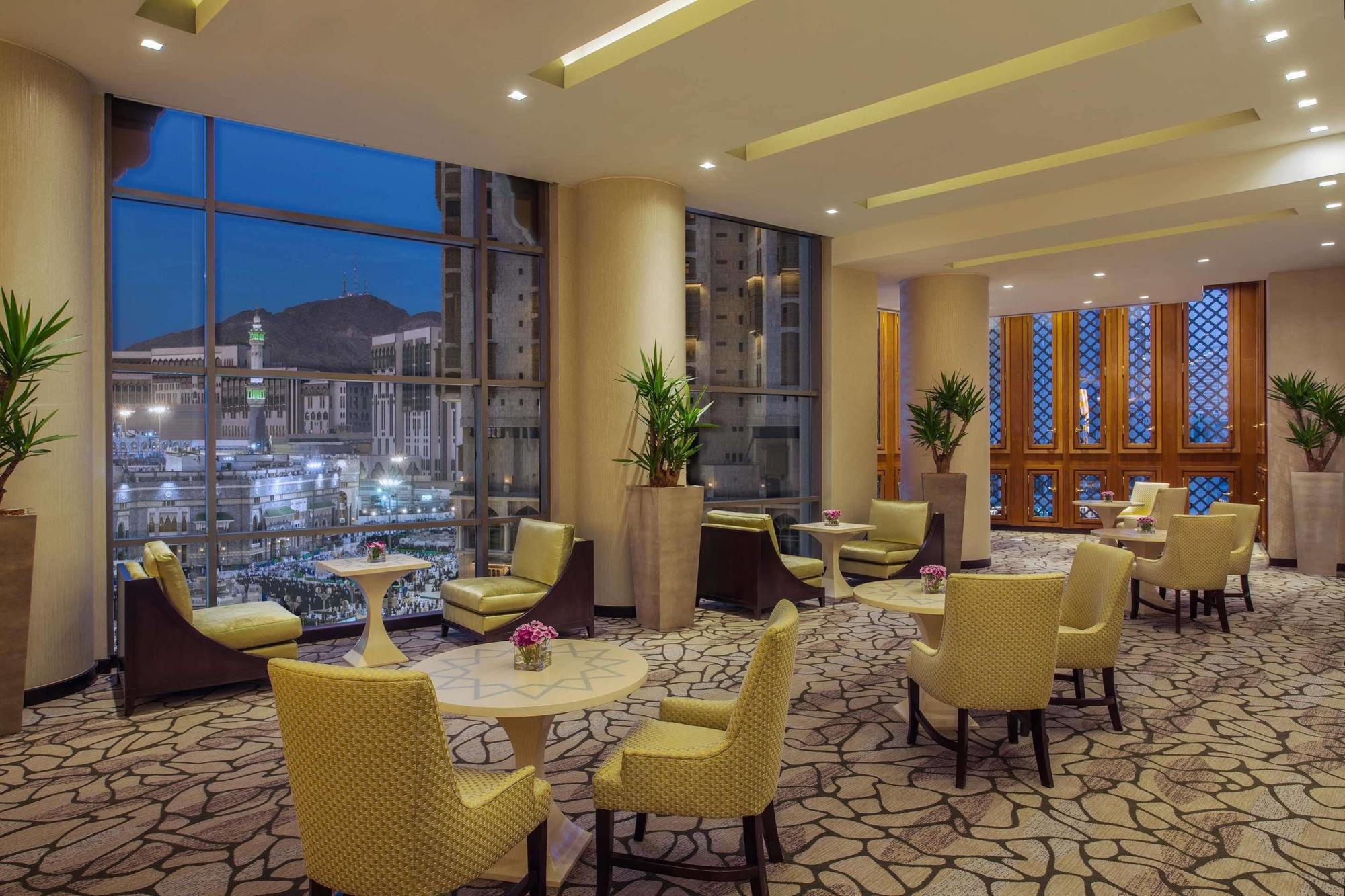 Hotel Jabal Omar Hyatt Regency Makkah La La Mecca Esterno foto The photo shows a stylish lounge area, likely located in a hotel or café. It features several comfortable seating arrangements with light-colored chairs and small tables. The space is well-lit with modern lighting and has large windows that offer a v