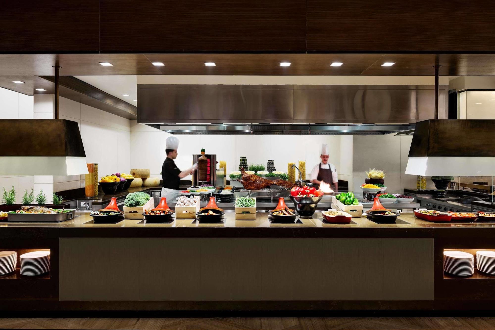 Hotel Jabal Omar Hyatt Regency Makkah La La Mecca Esterno foto The photo shows a well-organized kitchen or buffet area. In the foreground, there are several food stations displaying a variety of dishes, including fresh vegetables, meats, and other culinary items arranged in bowls or trays. Behind the counter, tw