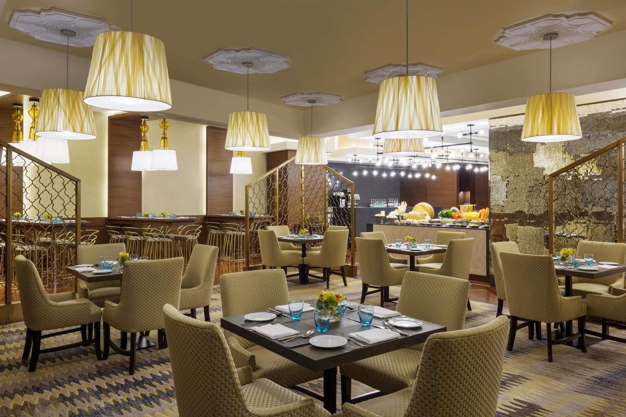 Hotel Jabal Omar Hyatt Regency Makkah La La Mecca Esterno foto The photo displays a modern restaurant interior. It features a series of round tables with beige upholstered chairs arranged neatly throughout the space. Each table is set with plates and blue-tinted glasses. The lighting is provided by stylish penda