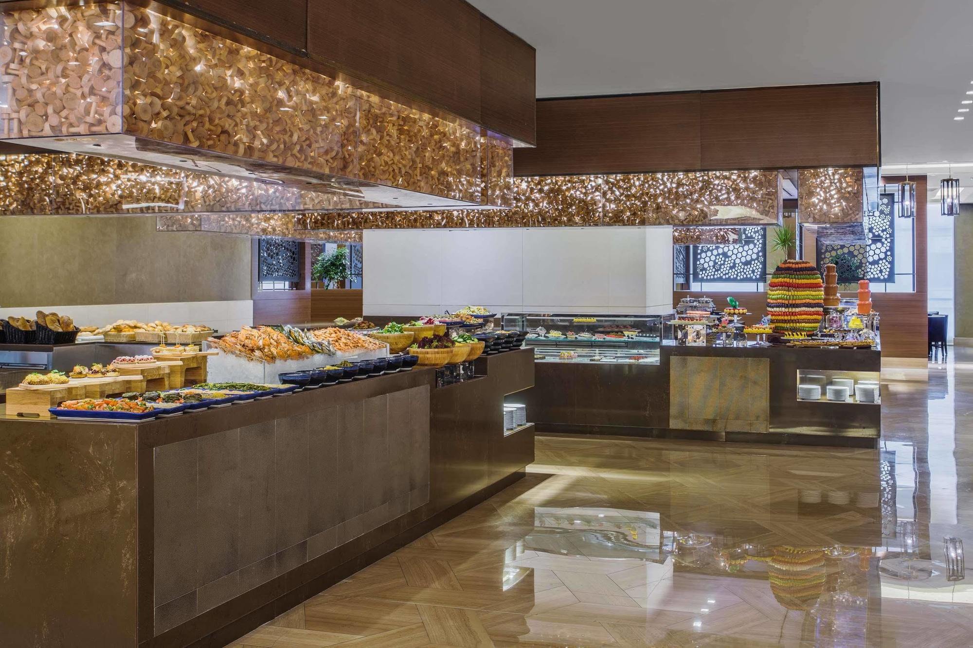 Hotel Jabal Omar Hyatt Regency Makkah La La Mecca Esterno foto The photo shows an elegant buffet setup in a spacious dining area. There are various food displays arranged on sleek surfaces, including an assortment of items such as pastries, fruits, and possibly other dishes. The decor features warm lighting with