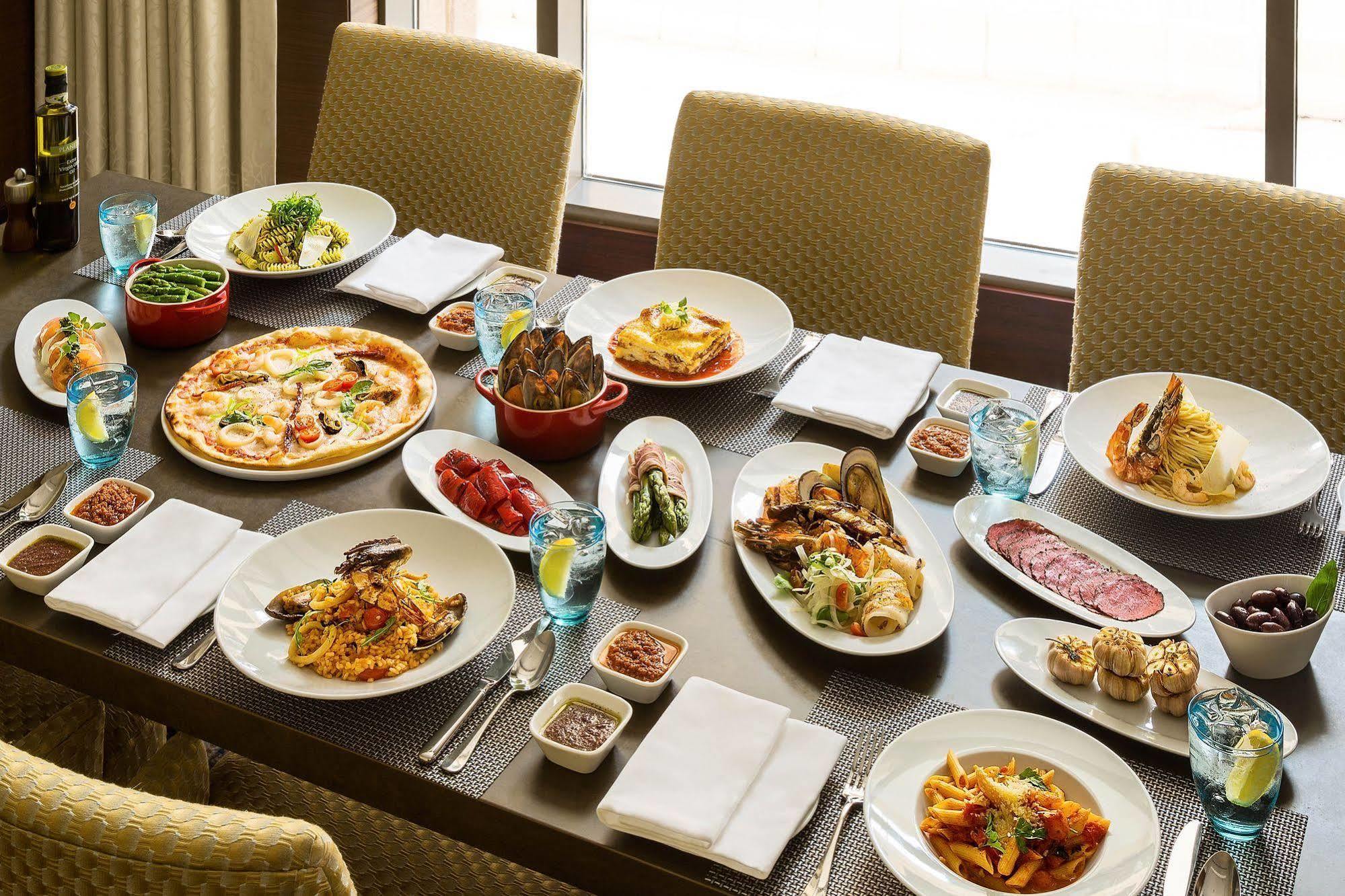 Hotel Jabal Omar Hyatt Regency Makkah La La Mecca Esterno foto The photo shows a large dining table set with various dishes, suggesting a festive or communal meal. There are several plates of food including:

- A pizza topped with vegetables and possibly meats.
- A serving of lasagna.
- A variety of pasta dishes