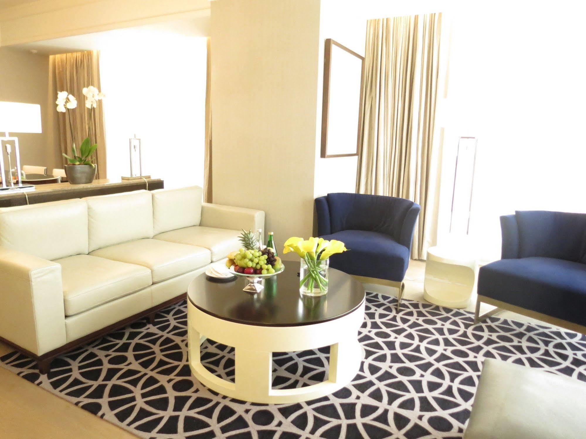 Hotel Jabal Omar Hyatt Regency Makkah La La Mecca Esterno foto The photo shows a stylish and modern living area. It features a white sectional sofa, two blue upholstered chairs, and a round black coffee table with a decorative centerpiece that includes flowers and fruits. The flooring is covered with a patterned