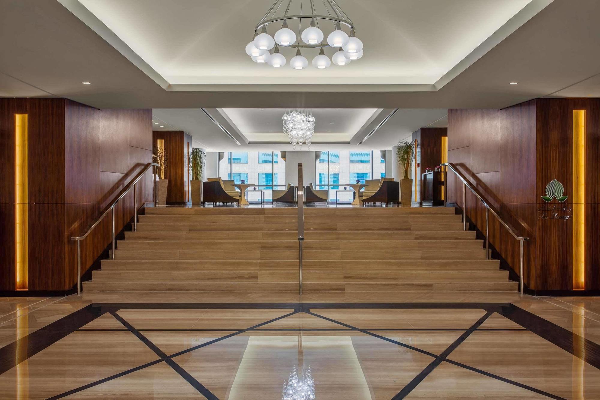 Hotel Jabal Omar Hyatt Regency Makkah La La Mecca Esterno foto The photo depicts a modern and elegant lobby area. There is a wide staircase made of wood that leads up to another level, flanked by stylish seating on both sides. The lobby features a combination of wooden and marble flooring, with a geometric patte