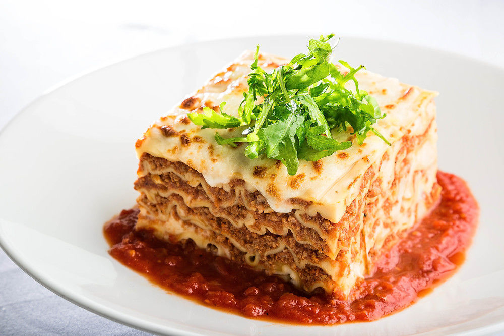 Hotel Jabal Omar Hyatt Regency Makkah La La Mecca Esterno foto The photo shows a serving of lasagna, which is a layered pasta dish. The lasagna has multiple layers, with a combination of meat, cheese, and béchamel sauce, topped with a sprinkle of fresh green herbs. It sits on a plate with a rich red tomato sauce