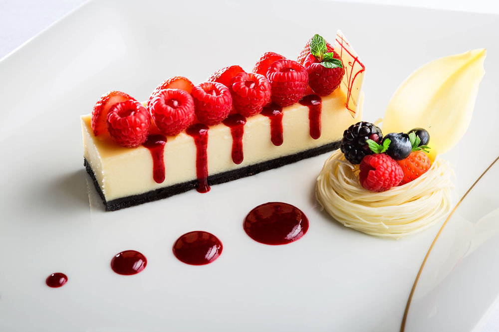 Hotel Jabal Omar Hyatt Regency Makkah La La Mecca Esterno foto The photo shows an elegantly plated dessert featuring a rectangular piece of cheesecake topped with fresh raspberries. The cheesecake is set on a dark crust, possibly made of chocolate or cookie crumbs. There are red fruit coulis drizzled artfully ar