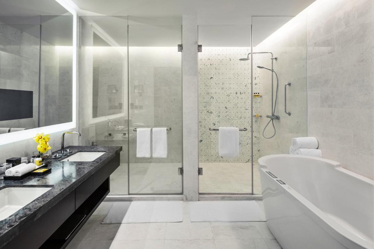 Hotel Jabal Omar Hyatt Regency Makkah La La Mecca Esterno foto The photo shows a modern bathroom with a sleek design. It features a glass shower enclosure with a rainfall showerhead and a stylish bathtub. The floor and walls have a light-colored stone or tile finish, giving a clean and minimalist look. There's a