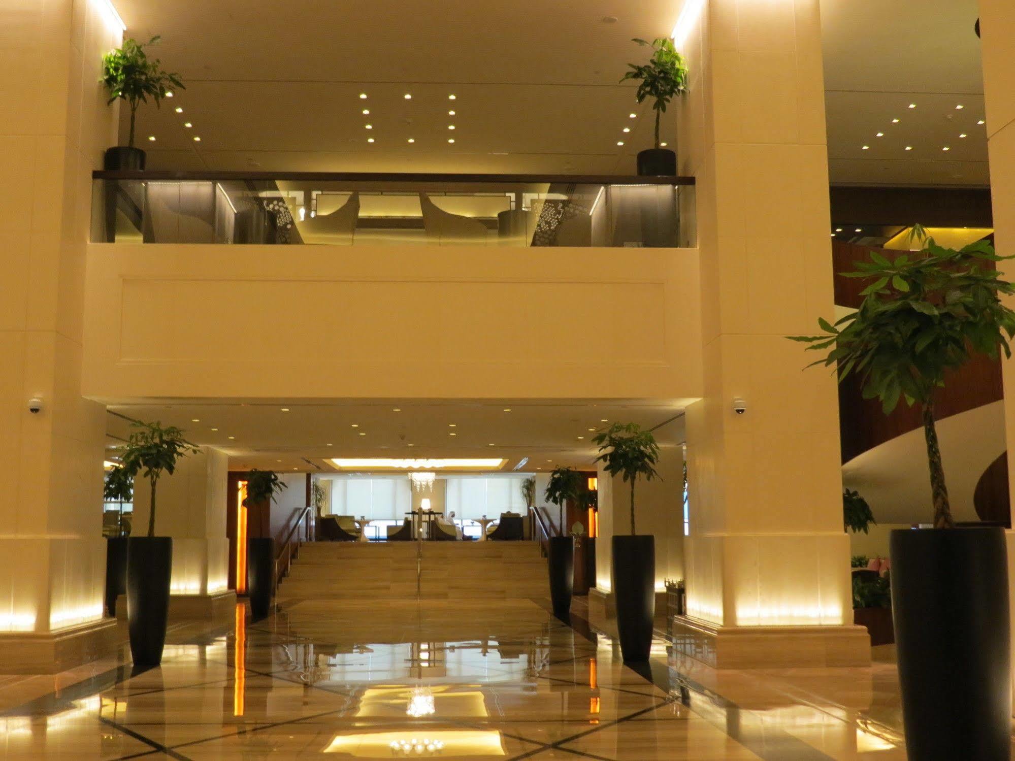 Hotel Jabal Omar Hyatt Regency Makkah La La Mecca Esterno foto The photo shows a spacious and elegantly designed hotel lobby. It features a multi-level layout with a set of stairs in the center leading to an upper floor. The lobby is well-lit with a warm glow from recessed lighting, and there are decorative plan