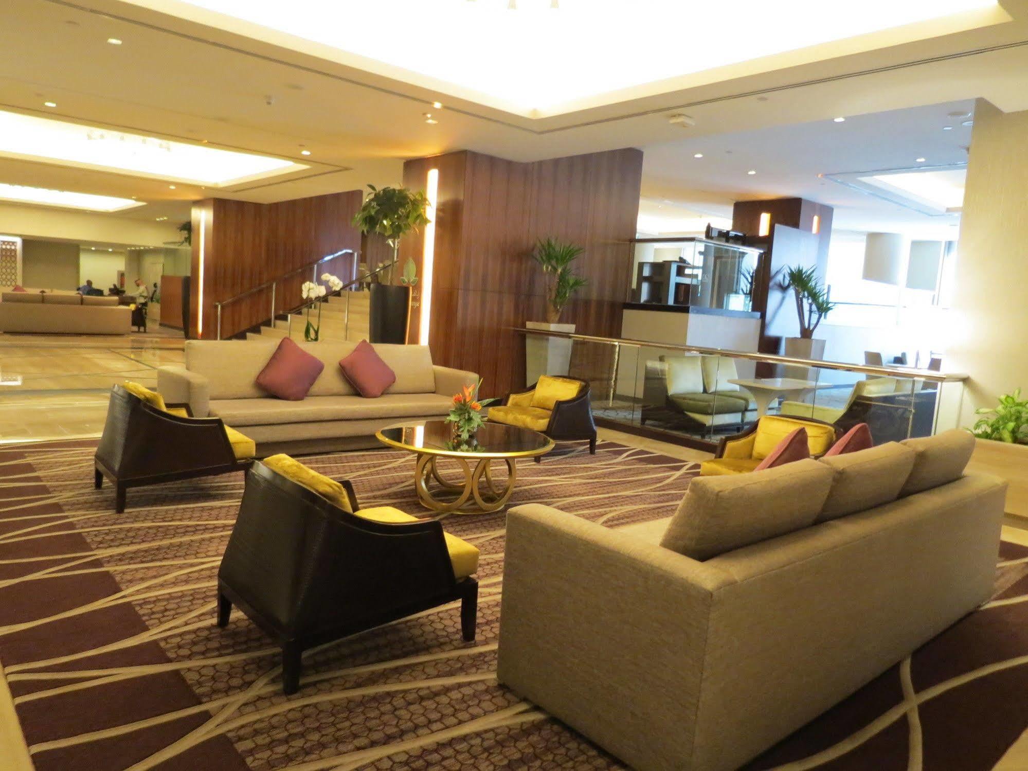 Hotel Jabal Omar Hyatt Regency Makkah La La Mecca Esterno foto The photo shows a modern and stylish lobby or lounge area. It features two large sofas with a light color and several cushions in shades of purple. There are also two armchairs with a darker finish and yellow cushions. In the center, there is a round
