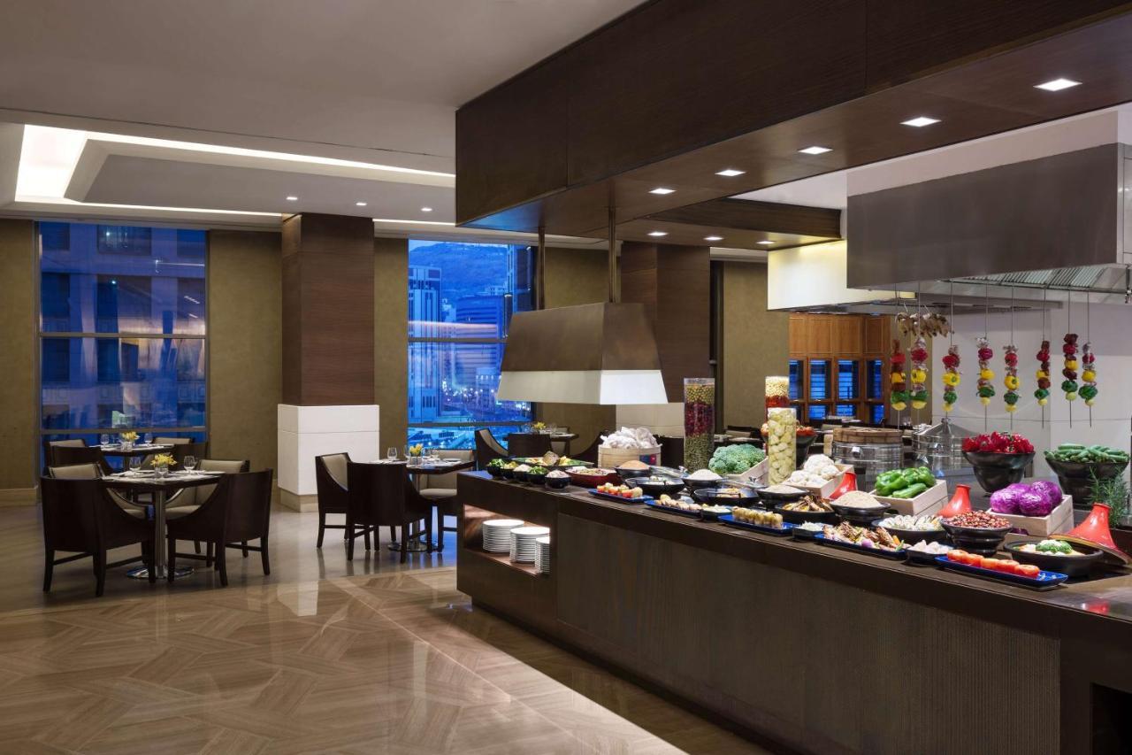Hotel Jabal Omar Hyatt Regency Makkah La La Mecca Esterno foto The photo shows a dining area, likely within a restaurant or buffet setting. On the right side, there is a long food display featuring various dishes, likely consisting of fruits, vegetables, and other culinary items. The area is well-lit, with moder