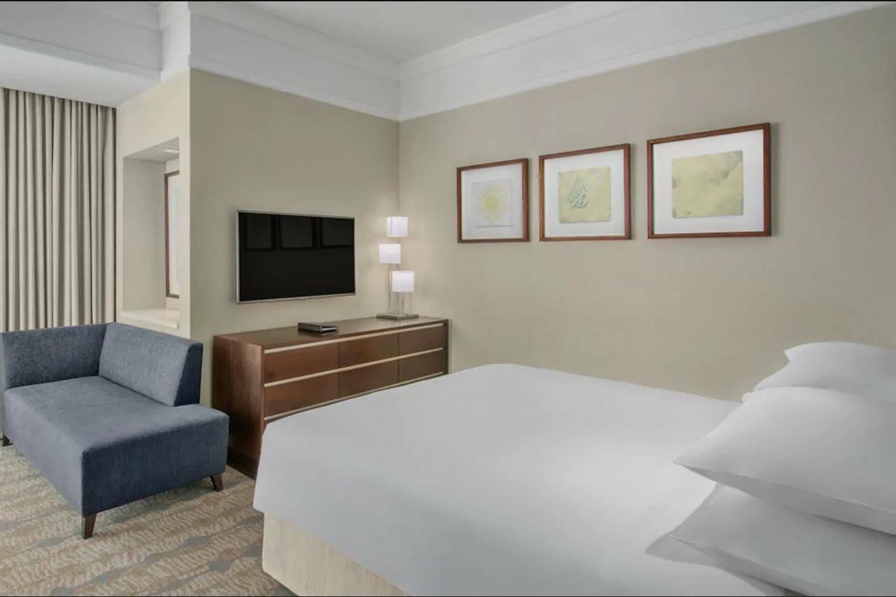 Hotel Jabal Omar Hyatt Regency Makkah La La Mecca Esterno foto The photo shows a modern hotel room. It features a neatly made bed with white linens and multiple pillows. On the wall opposite the bed, there is a flat-screen television mounted, along with a modern wooden dresser. Above the dresser, three framed ar