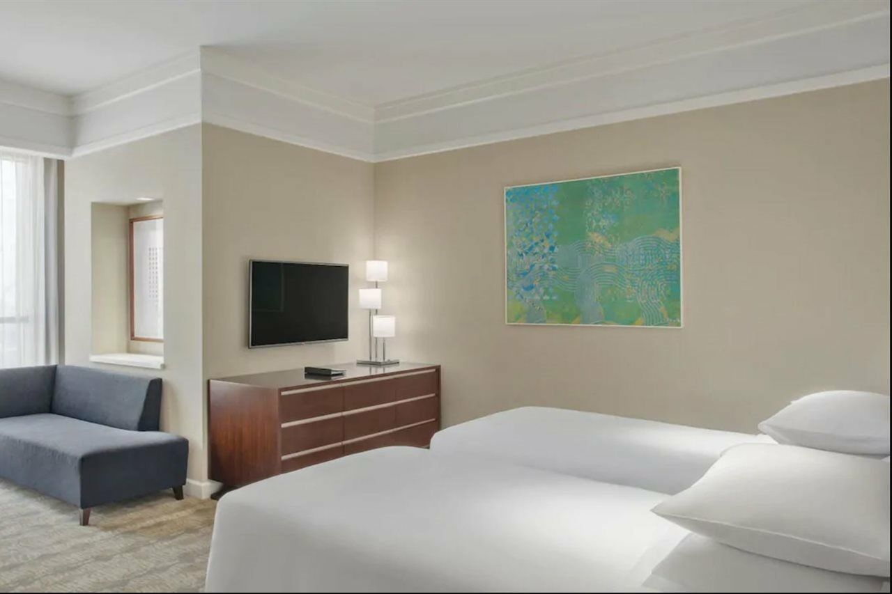 Hotel Jabal Omar Hyatt Regency Makkah La La Mecca Esterno foto The photo shows a hotel room featuring two twin beds with white bedding. A dark wooden dresser is positioned against one wall, with a flat-screen TV mounted above it. Next to the dresser, there are two modern lamps providing soft lighting. On the wal