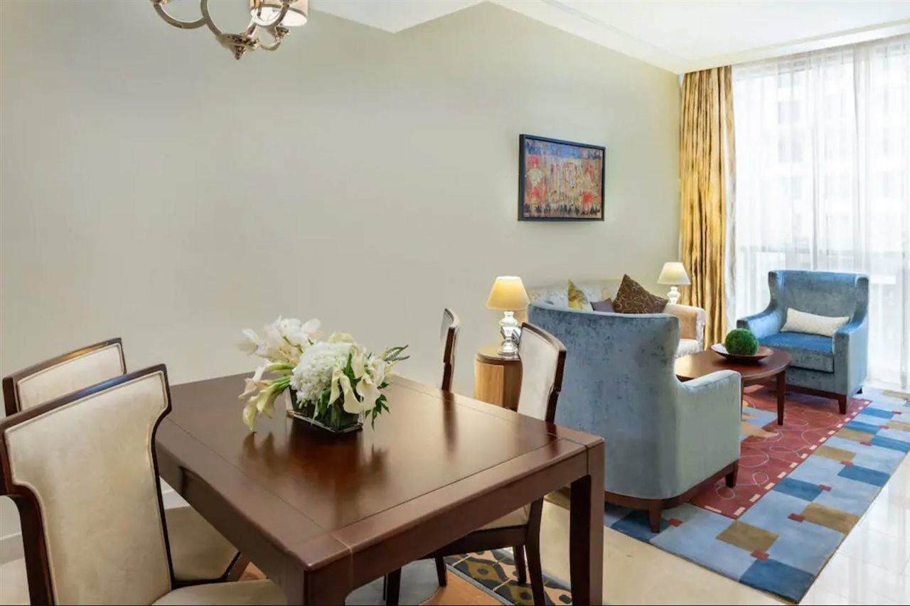 Hotel Jabal Omar Hyatt Regency Makkah La La Mecca Esterno foto The photo shows an elegantly furnished living space. On the left, there's a wooden dining table with four chairs, decorated with a vase of white flowers. To the right, there are two comfortable blue armchairs and a small side table, each adorned with